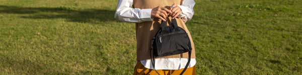 A person lies amidst colorful confetti and wrapped gift boxes, wearing a black outfit with a small black handbag placed near them, creating a festive atmosphere.