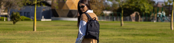 A person walking outdoors wearing a green and white striped shirt and carrying a sleek black backpack, with a storefront and posters visible in the background.