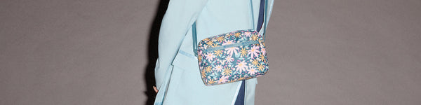 A seated individual wearing yellow patterned pants, a white lace blouse, and brown shoes, carrying a small black crossbody bag in an indoor setting