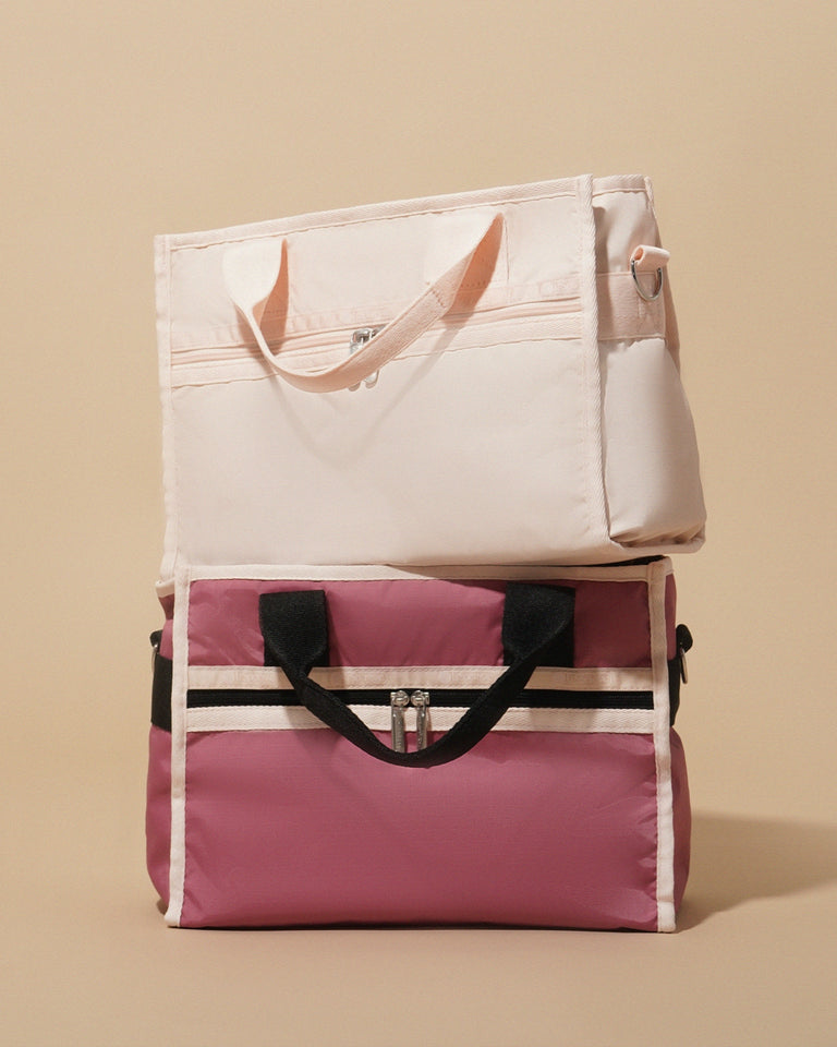 Two stylish LeSportsac nylon tote bags are stacked against a neutral beige background. The top bag is a soft peach pink with matching handles, while the bottom bag is a deeper mauve with contrasting black and pale peach straps and zipper details.